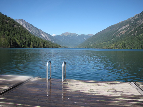 Beautiful lake view located at Birkenhead Lake, British Columbia.  Dock looking out into the water with mountain views and surrounded by forest on a sunny summer day.