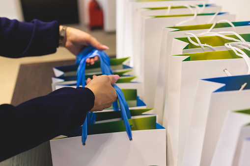 Corporate gifts and souvenirs presentation for company employees, gift bag package for conference participants before start, gift giving at office work, white and green paper bags with a blue ribbon
