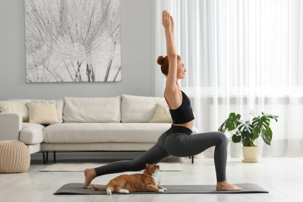istock Young woman with cute red cat practicing yoga on mat at home 1940930253