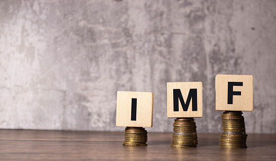 Stacks of gold coins with the letters IMF (International Monetary Fund) on a wooden cube. Business concept.