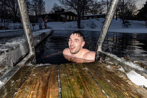 Stockholm, Sweden Jan 5, 2024 A young man  ice bathing from a dock into a frozen lake.