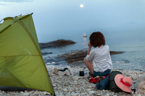 Woman Camping on a Beach Enjoying Moon Rising over Sea in Tranquility
