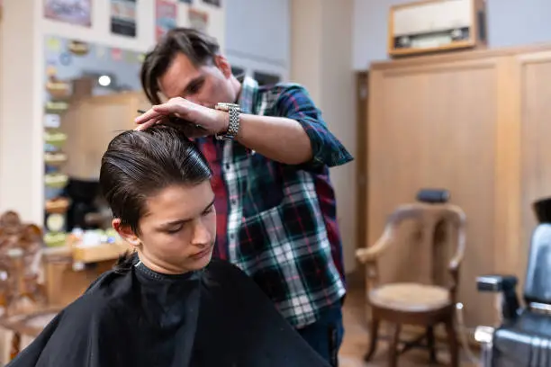 A hairdresser cuts a teenager's hair and gives him a modern haircut in an old-fashioned, retro-decorated hair salon.