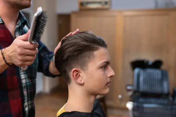 A hairdresser cuts a teenager's hair and gives him a modern haircut in an old-fashioned, retro-decorated hair salon.