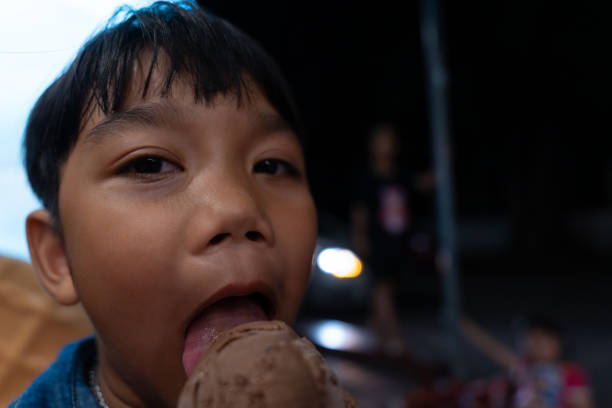 primo piano bambino asiatico che mangia un gelato al cioccolato in un cono di cialda. - child chocolate ice cream human mouth foto e immagini stock