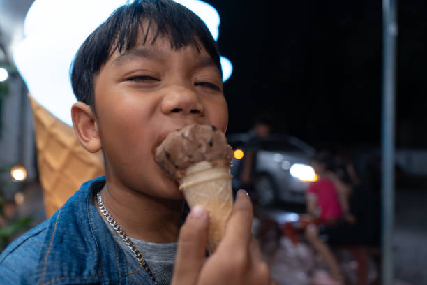 close-up asian child boy eating a chocolate ice cream in a waffle cone. - child chocolate ice cream human mouth foto e immagini stock