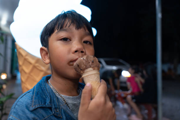 close-up asian child boy eating a chocolate ice cream in a waffle cone. - child chocolate ice cream human mouth foto e immagini stock
