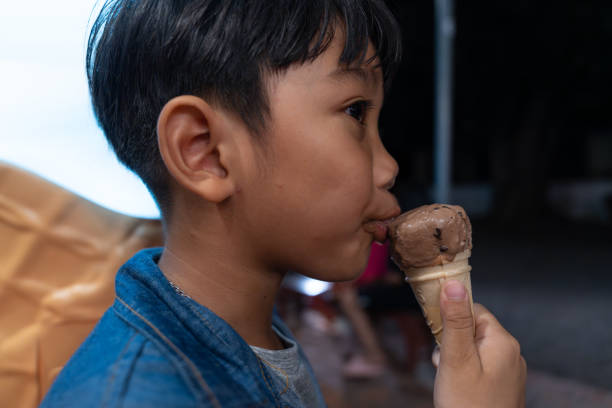 primo piano bambino asiatico che mangia un gelato al cioccolato in un cono di cialda. - child chocolate ice cream human mouth foto e immagini stock