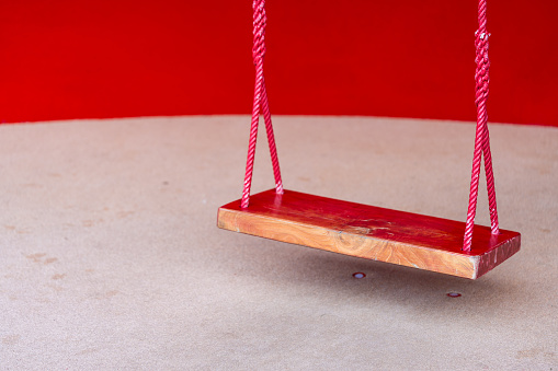 Wooden red swing for entertaining the smallest boys and girls. The empty red swing