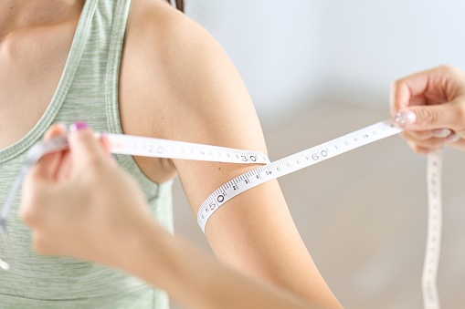 A woman measuring the circumference of her arm with a tape measure