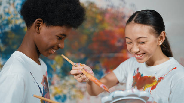 istock Smiling diverse children paint color on each other shirt at wall. Edification. 1941317578