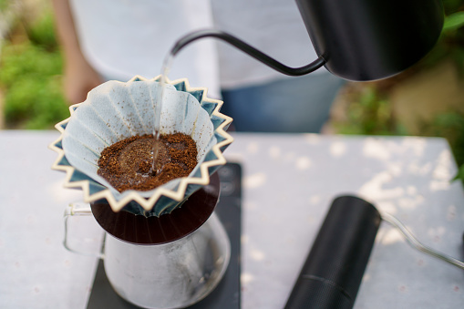 Happy Asian beautiful woman making a specialty coffee in morning at her backyard garden, woman brewing a coffee by dripping or pouring over a hot water.