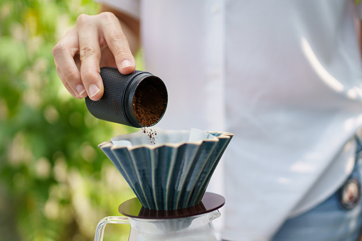 Happy Asian beautiful woman making a specialty coffee in morning at her backyard garden, woman brewing a coffee by dripping or pouring over a hot water.