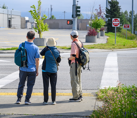 Three people waiting at the intersection. Red hand pedestrian stop sign on display. Anchorage. Alaska. USA.