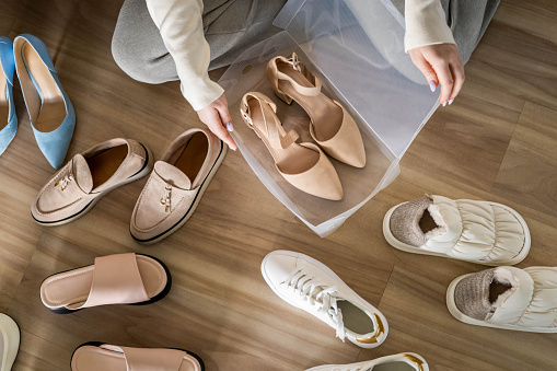 Woman hands packing beige shoes on heels into plastic box for comfortable storage organize top view. Female putting feminine footwear to PVC container on floor contemporary tidying up arrangement