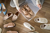 Woman hands packing beige shoes on heels into plastic box for comfortable storage organize top view