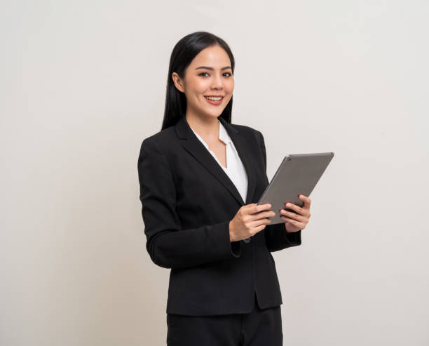 istock Attractive elegant young asian business woman using digital tablet standing on isolated background. Happy young latin female formal black suit holding tablet gadget working service with customer 1941415890