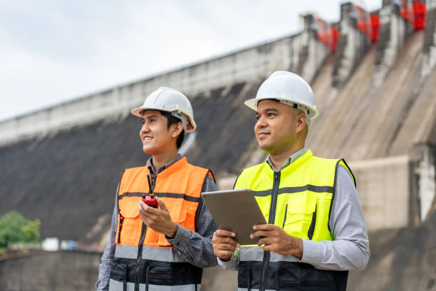 istock Confident asian two maintenance engineers man inspection discussstion with tablet at construction site dam with hydroelectric power plant and irrigation. Team engineer man working at project 1941416402