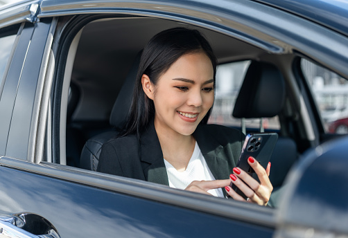 Young beautiful asian business women getting new car using smartphone while driving car. she very happy and excited with cell phone driving application. Business female vehicle on the road