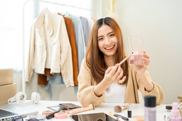istock Young beautiful asian woman vlogger live broadcasting cosmetic makeup tutorial content with eye shadow. Influencers professional beauty make up with various cosmetics recording video on social media 1941435539