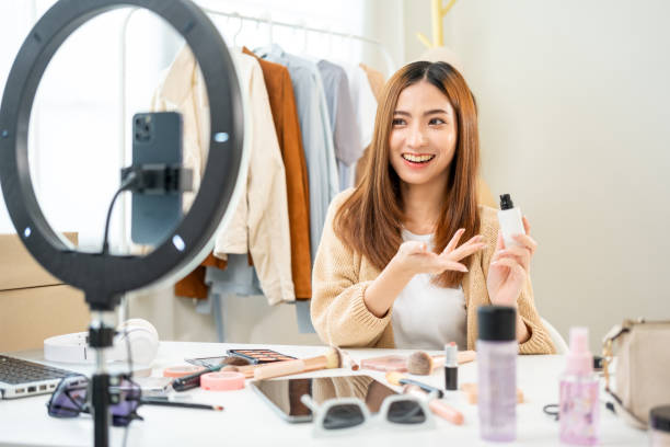 istock Young beautiful asian woman vlogger live broadcasting cosmetic makeup tutorial content with treatment moisturizer cream. Influencers with applying moisturizing skincare cream lotion review on social 1941435541