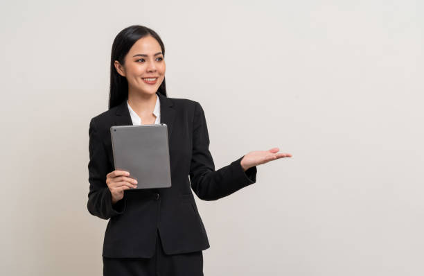 istock Attractive elegant young asian business woman using digital tablet standing on isolated background. Happy young latin female formal black suit holding tablet gadget working service with customer 1941461356