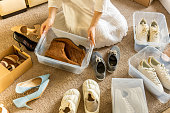 Woman arrangement shoes into plastic container and cardboard box seasonal storage organizing closeup