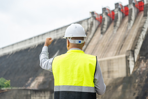 Professional asian maintenance engineer man with safety helmet in construction site dam with hydroelectric power plant and irrigation. Manager engineer man working at project big building.
