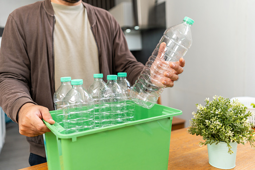 A young man arranged plastic bottles into a box. He assumes plastic bottles will sort of trash before throwing them into the bin. World environment day. Recycle waste reduce environmentally friendly