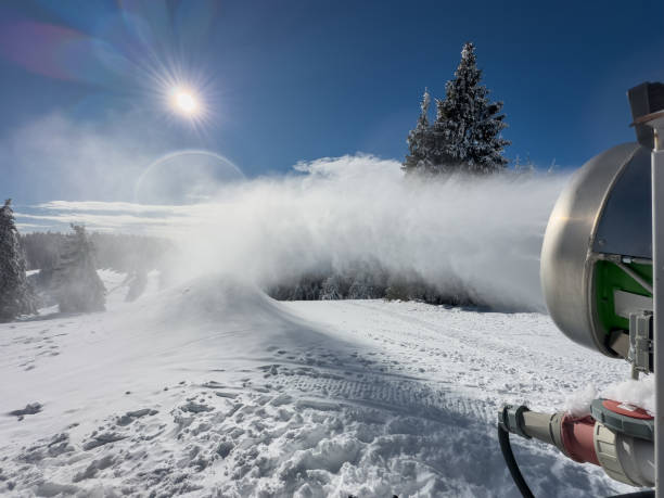 Close-up shot of snow canon spraying artificial snow on ski slope on sunny winter day