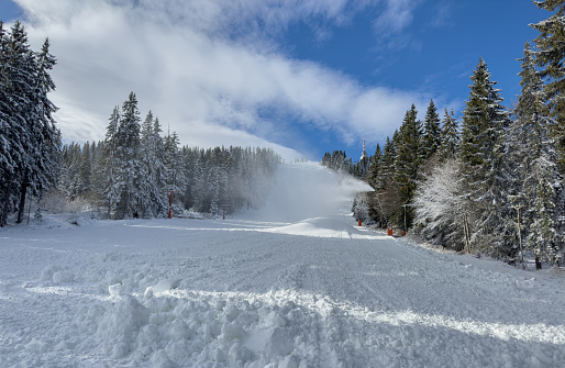 Snow canons spraying artificial snow on ski slope on sunny winter day