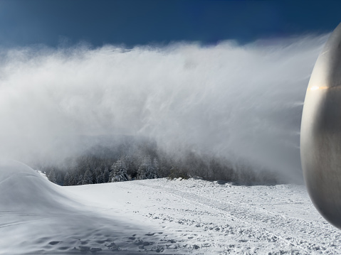 Close-up shot of snow canon spraying artificial snow on ski slope on sunny winter day