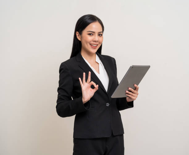 istock Attractive elegant young asian business woman using digital tablet standing on isolated background. Happy young latin female formal black suit holding tablet gadget working service with customer 1941498516