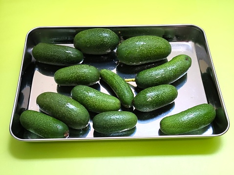A metal container holds fresh seedless avocados against a vibrant green backdrop, highlighting their natural allure and inviting freshness.