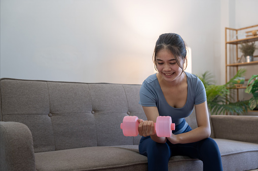 Young Asian woman exercise with dumbbells at home.