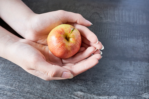 Female hands holding a red apple on a wooden background. Healthy eating concept.