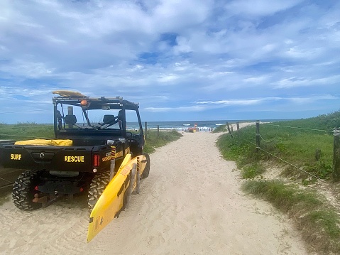 Horizontal summer seascape of surf life saving truck with rescue surfboard at beach sand dune path entrance under a cloudscape sky at Brunswick Heads beach NSW Australia