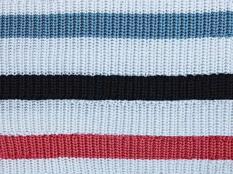 Texture of white woolen fabric with blue and pink stripes. Knitted texture of clothes, close-up view