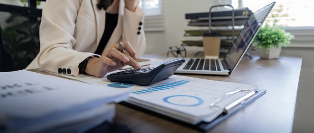 Businesswoman accountant using calculator and laptop for matching financial data saving in office room, Business financial, tax, accounting concept.