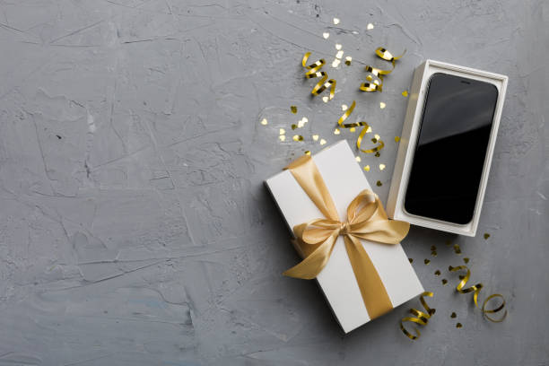 istock Opened gift box with gold ribbon and smartphone on color background, top view. Blank open box packaging mockup , Template for your design - branding mockup 1941679435