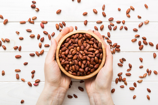 Woman hands holding a wooden bowl with peanuts. Healthy food and snack. Vegetarian snacks of different nuts.