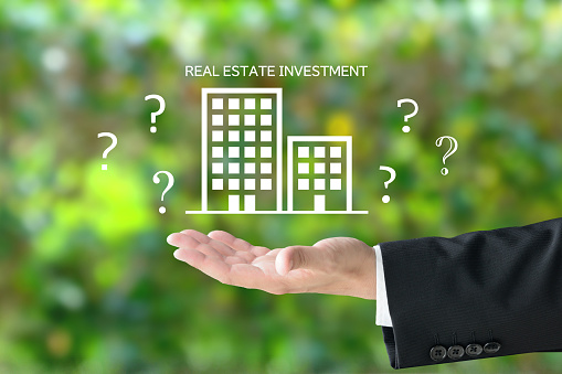 Business man's hand and building pictogram and REAL ESTATE INVESTMENT word with question marks