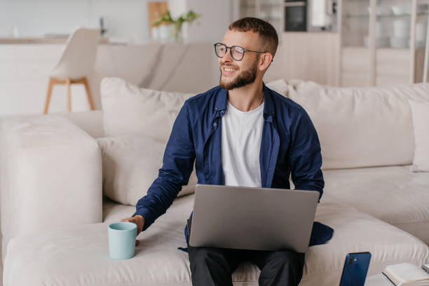 istock Smiling man with laptop and coffee mug on a comfortable couch 1941758852