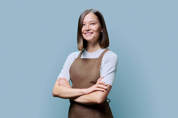 istock Young smiling woman in apron looking at camera on blue studio background 1941763118