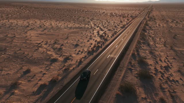 Car driving on a desert highway near Valley of the Gods and Monument Valley in Utah and Arizona. Modern black SUV automobile on road aerial drone point of view in cinematic red sandstone rock formation landscape. Blue sky in Western USA, Wild West movie