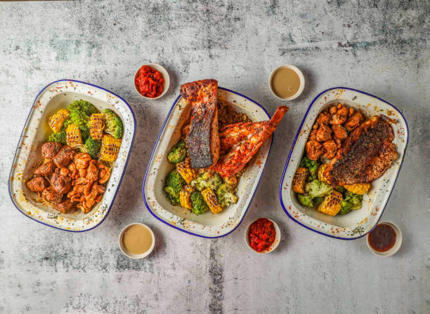 assorted grills grilled salmon, lobster tail, grill sea,bass fish, shrimps and chicken with fried rice, grilled corn and broccoli served in isolated on grey background top view of singaporean food - sea bass prepared fish food grilled imagens e fotografias de stock