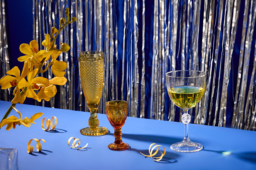 Blue surface with sparkling silver string background. Wine glasses, yellow orchids and ribbons decorated the table. The space is viewed from the front for advertising.