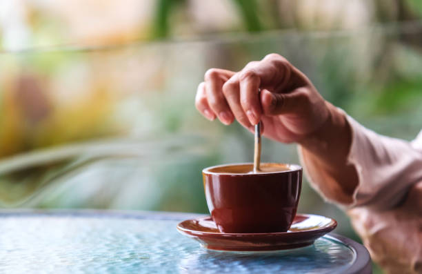 istock Woman's hands holding a spoon and stirring hot coffee on the table 1941828394