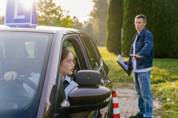 istock Male instructor showing stop sign with clipboard in his hand while looking at how scared young lady parking in the driving school outdoors. Traffic cone near car. 1941830065