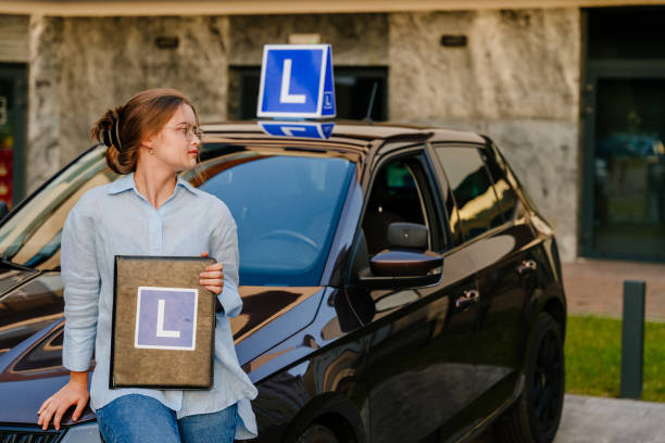 young charming female driver posing with l plate on the roof of car. driving school and people concept. young beautiful happy woman posing near training car - driving training car safety imagens e fotografias de stock